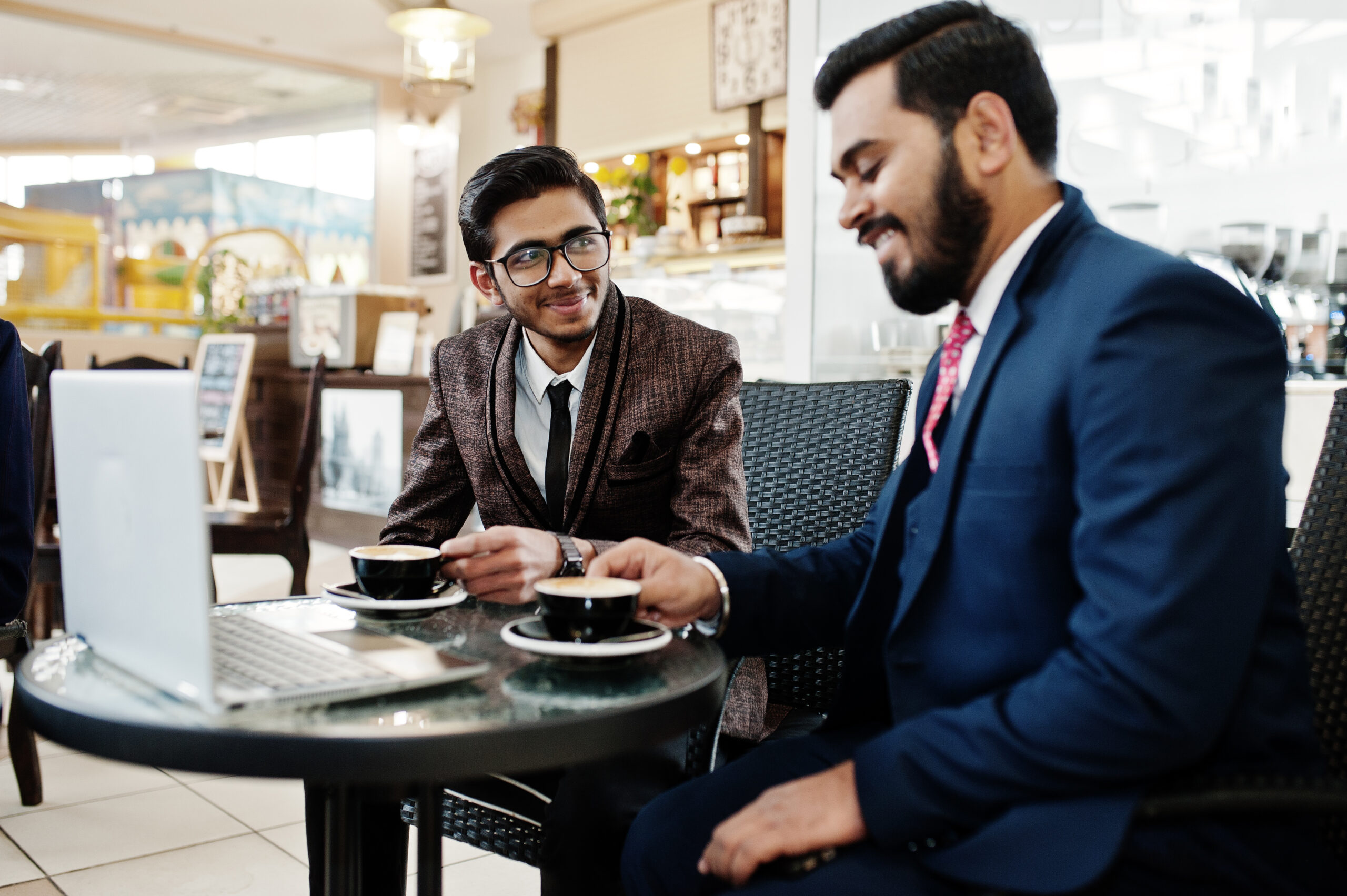 two indian business man in suits sitting at office on cafe, look